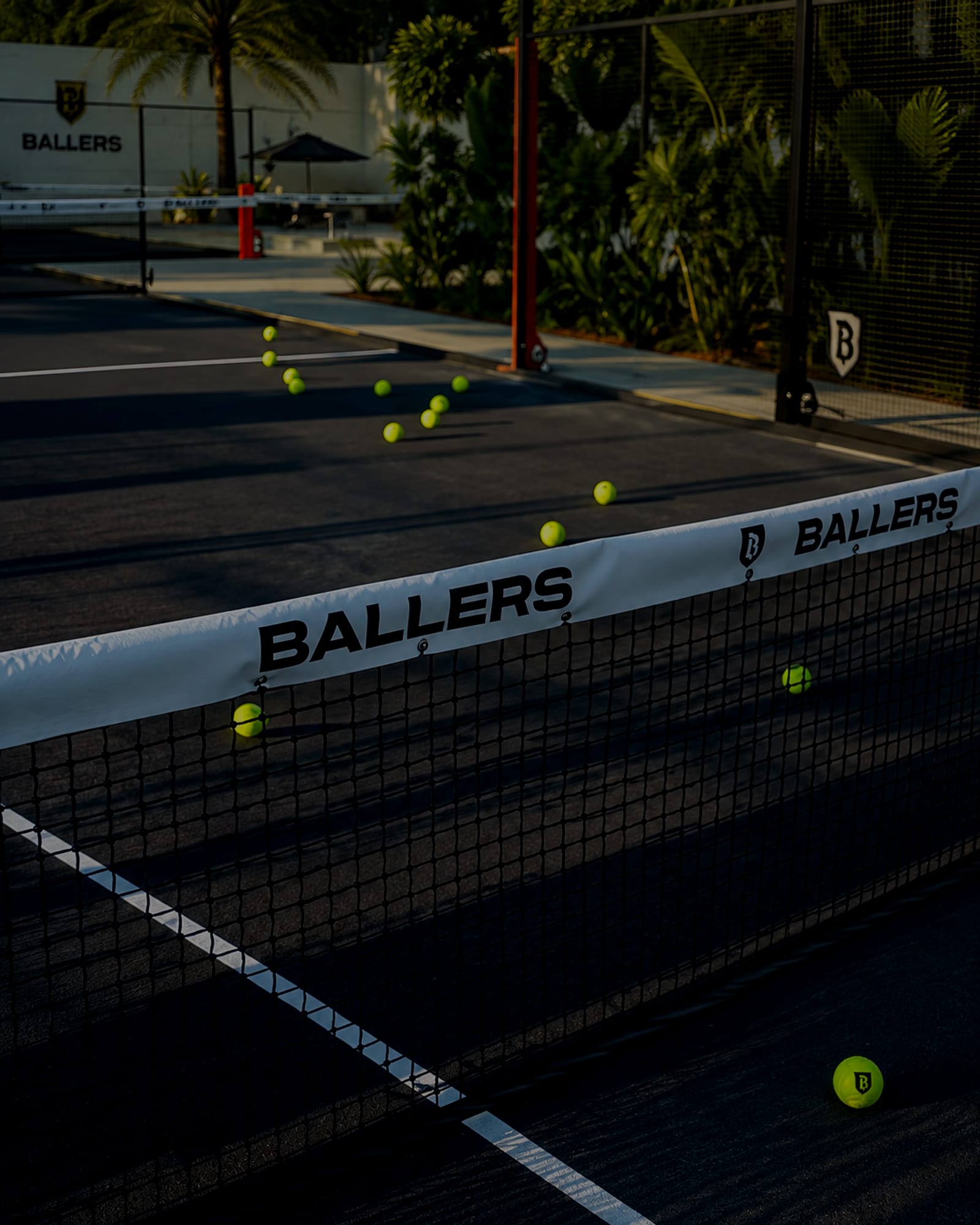The BALLERS net on a floodlit padel court, balls scattered across the surface behind it